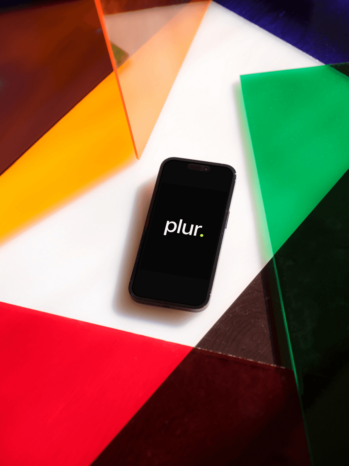 Plur Wallet phone mockup centred on a flat-lay of overlapping translucent colour panels